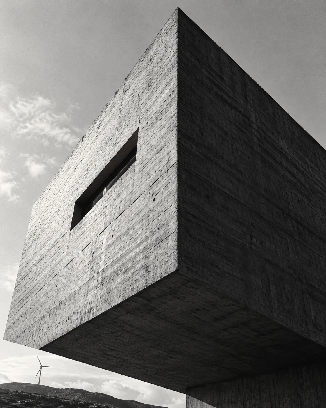 Looking up at the sharp corner of a cantilevered concrete volume against the sky.